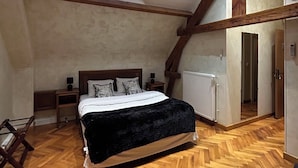 Een slaapkamer met houten vloer, een bed met een zwart dekbed, een nachtkastje, een klein tafeltje, een raam met uitzicht en een houten plafondbalk.