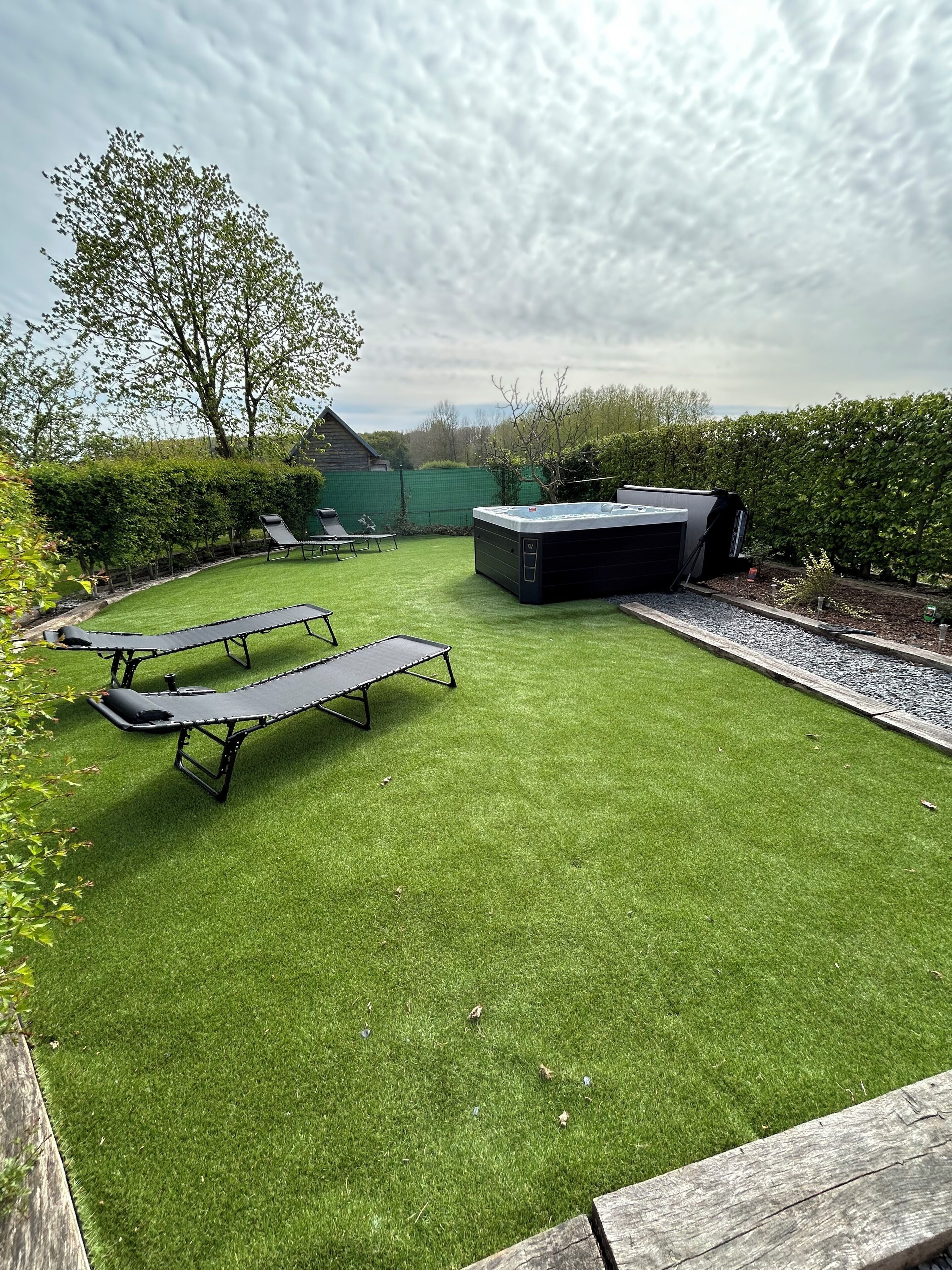 Un patio con césped artificial, un jacuzzi y una terraza de madera.
