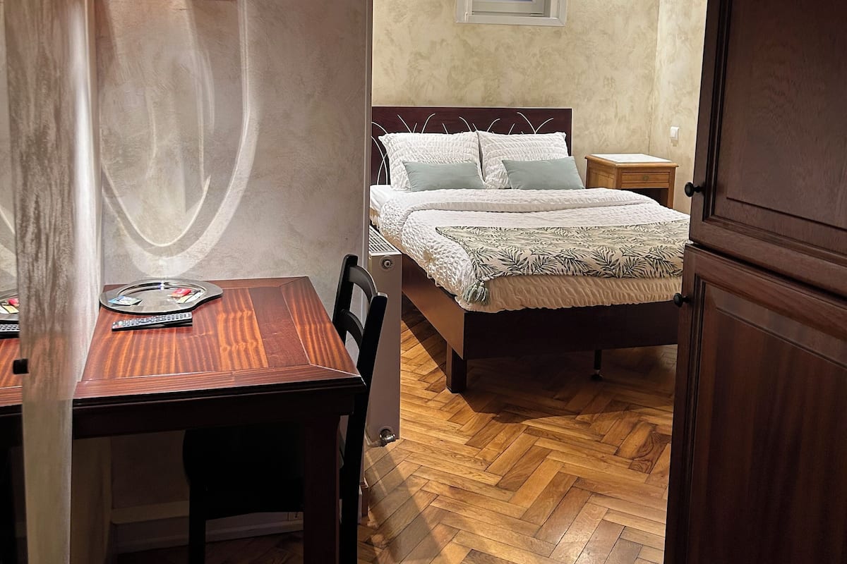 Une chambre à coucher de taille modeste, avec un lit en bois, une petite table de chevet et un bureau avec une chaise.
