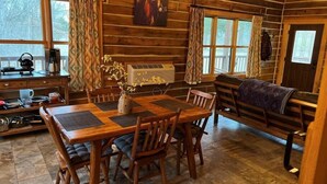 A cozy cabin interior with a wooden dining table, chairs, a bench, and a painting on the wall. - Contemporary Glamping with Native American Appeal (Anna)