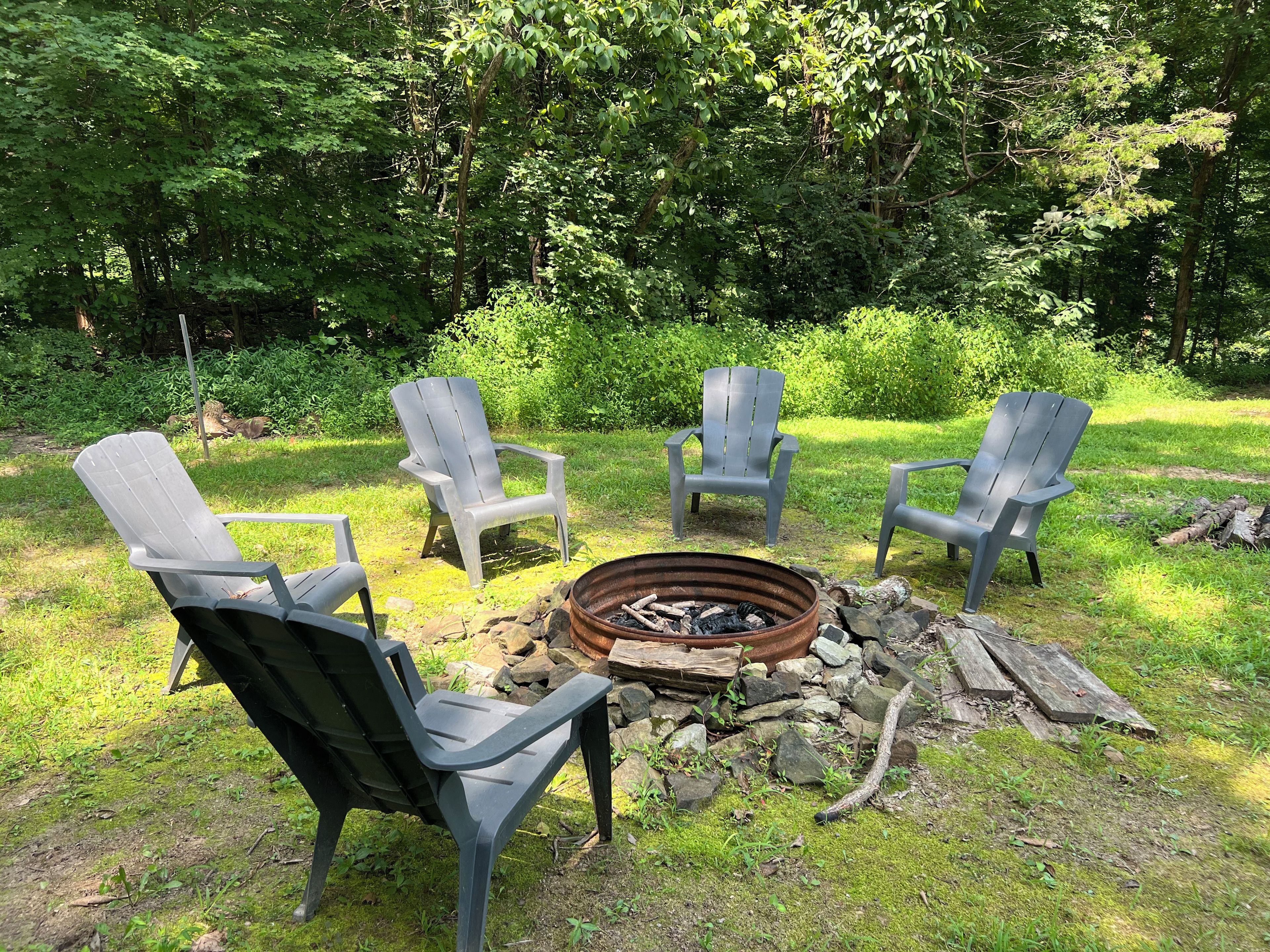 Un foyer est entouré de quatre chaises Adirondack dans un espace extérieur verdoyant.