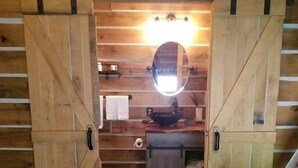 A rustic wooden room with a large mirror, wooden doors, and a small sink. - Contemporary Glamping with Native American Appeal (Anna)