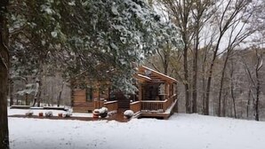 A wooden cabin with a porch and snow-covered ground. - Contemporary Glamping with Native American Appeal (Anna)