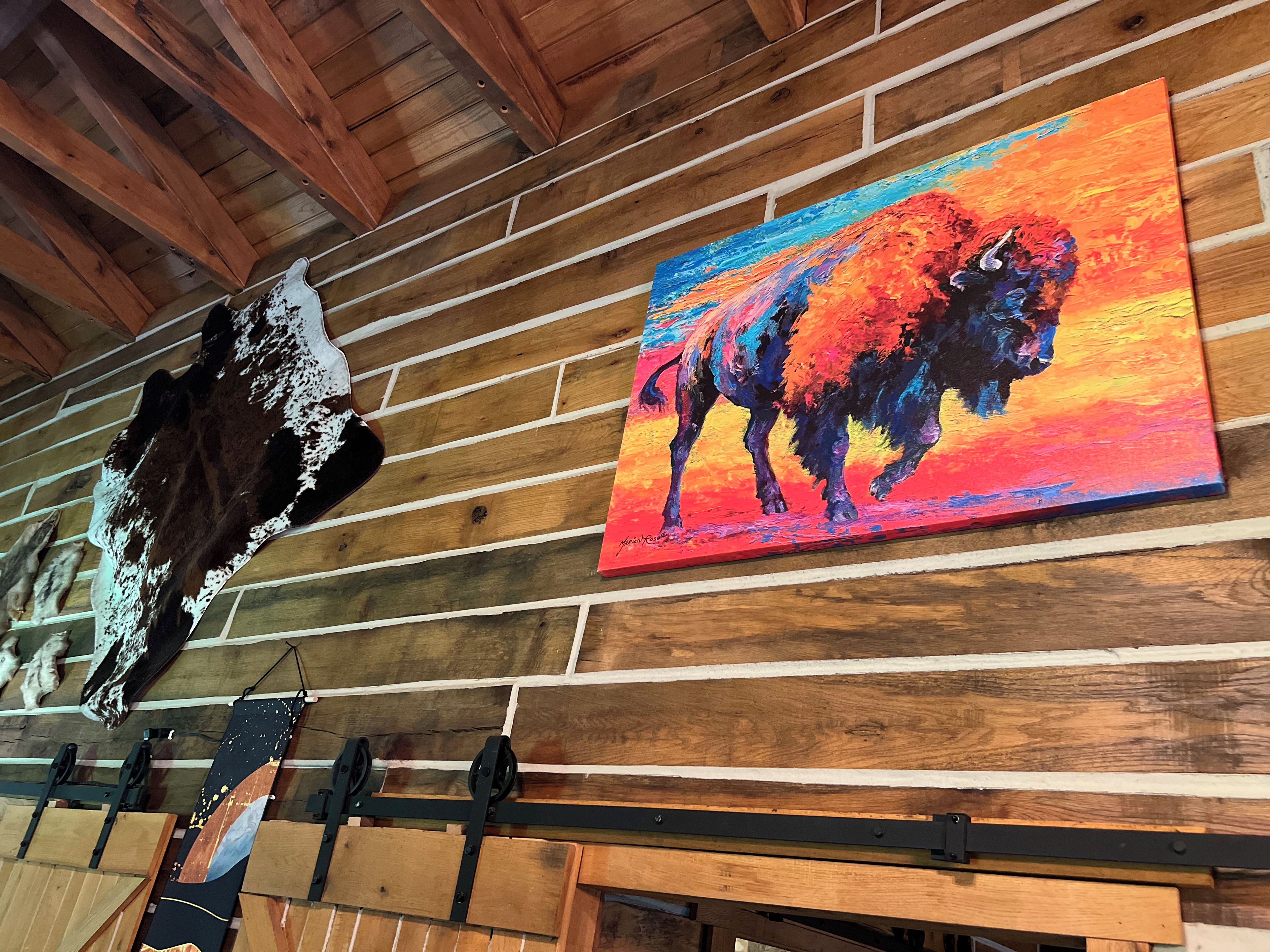 A wooden wall with a mounted painting of a bison and a mounted animal head.
