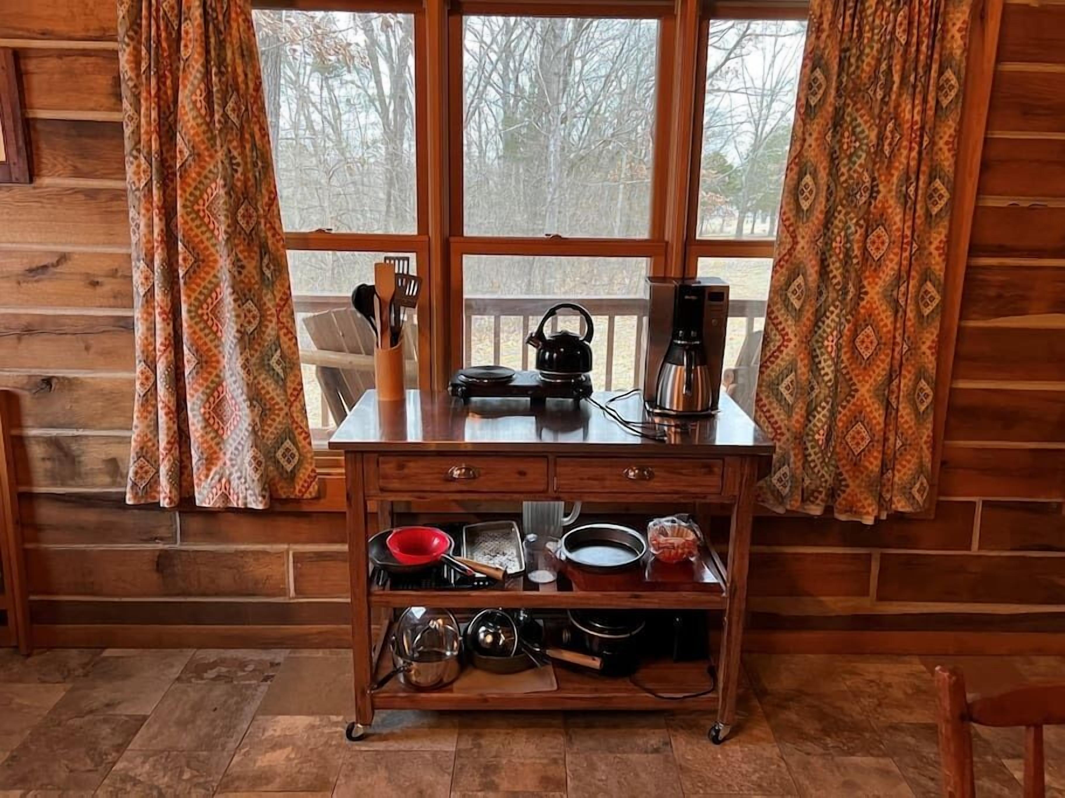 Interior de una cabaña de madera con mostrador de cocina, cafetera y diversos utensilios de cocina.