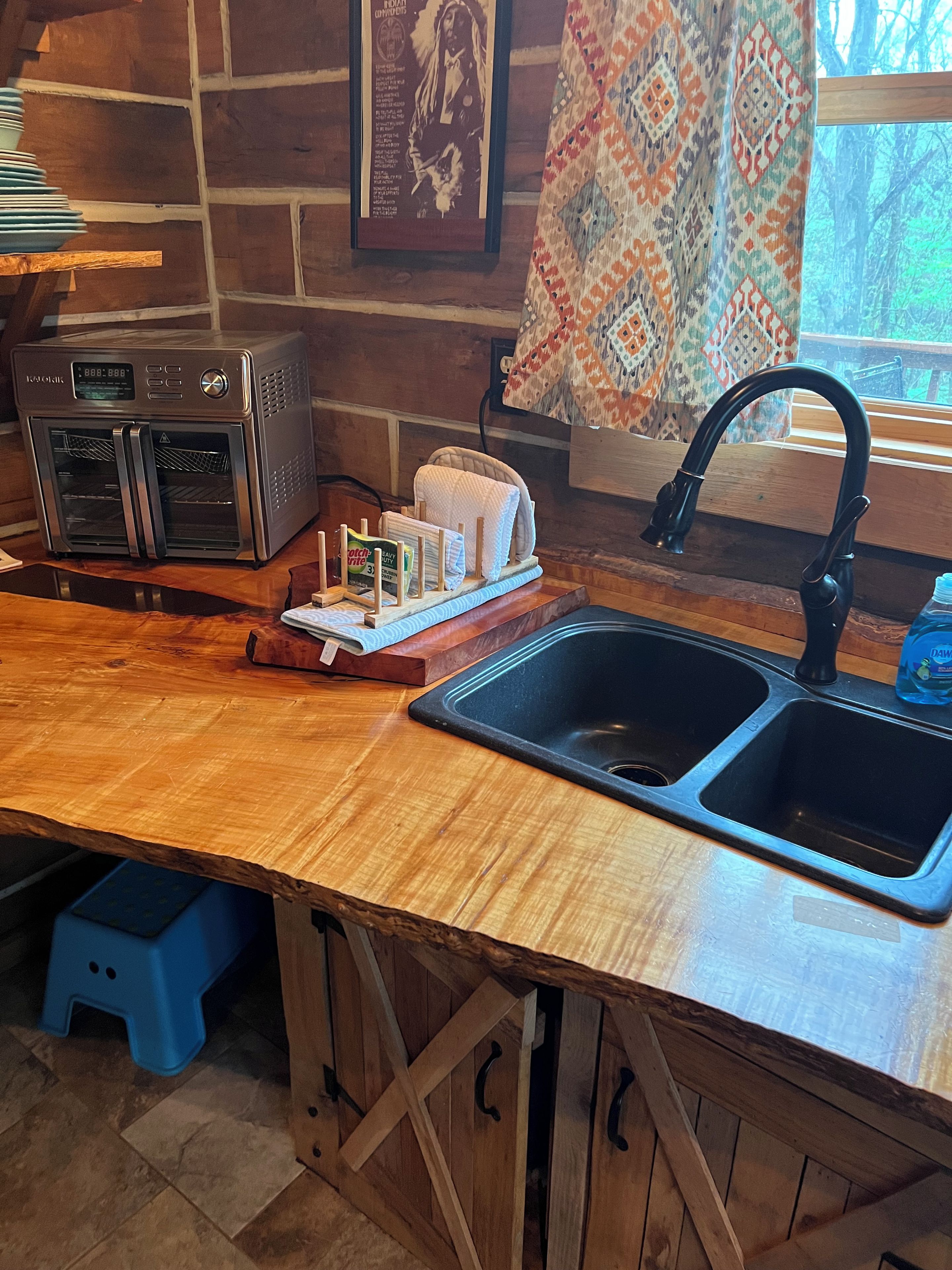 Una cocina con encimera de madera, un tostador, un fregadero y una ventana con cortinas estampadas.