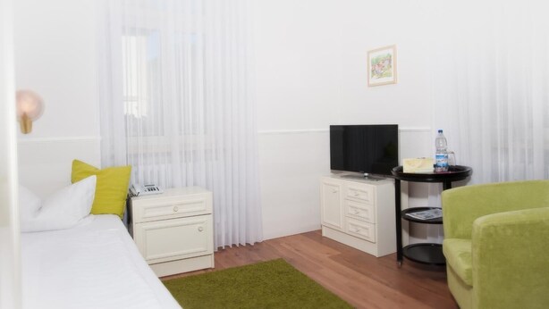 Ett hotellrum med en säng, en tv, ett litet bord med en vattenflaska och en grön stol.