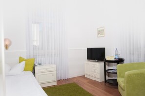Une chambre d’hôtel avec un lit, une télévision, une petite table avec une bouteille d’eau et une chaise verte.