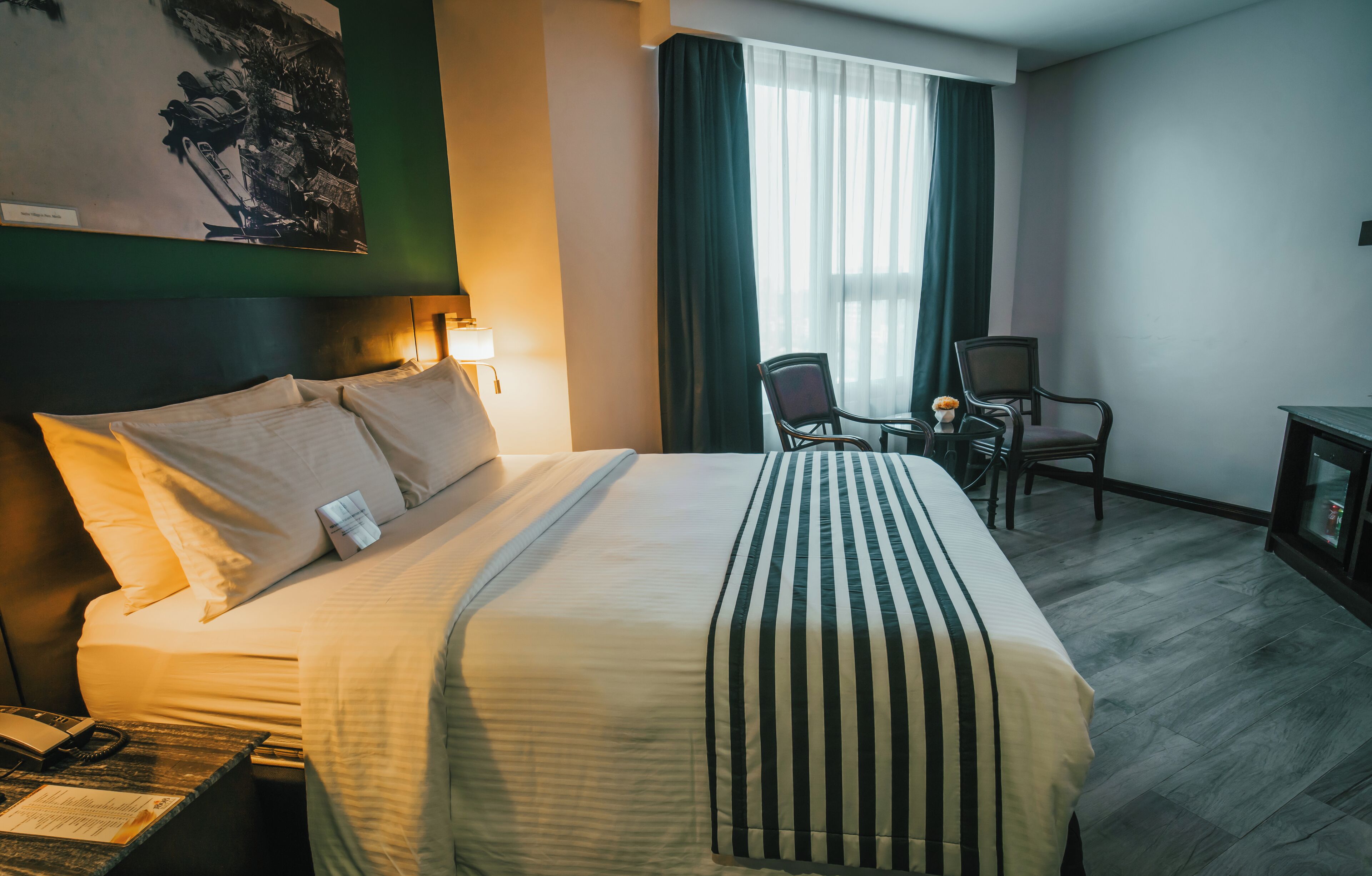 Une chambre d’hôtel avec un grand lit, un bureau avec une chaise, une petite table avec une chaise et une fenêtre avec des rideaux.
