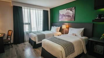 Habitación de hotel con dos camas, un escritorio, una silla, una pared de acento verde y un cuadro.