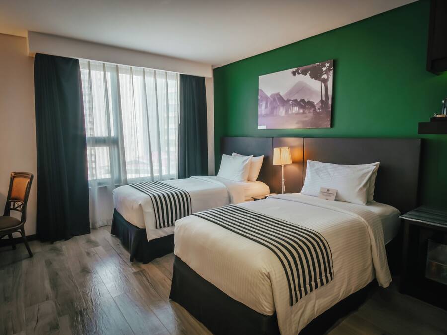 Une chambre d’hôtel avec deux lits, un bureau, une chaise, un mur d’accent vert et un tableau.