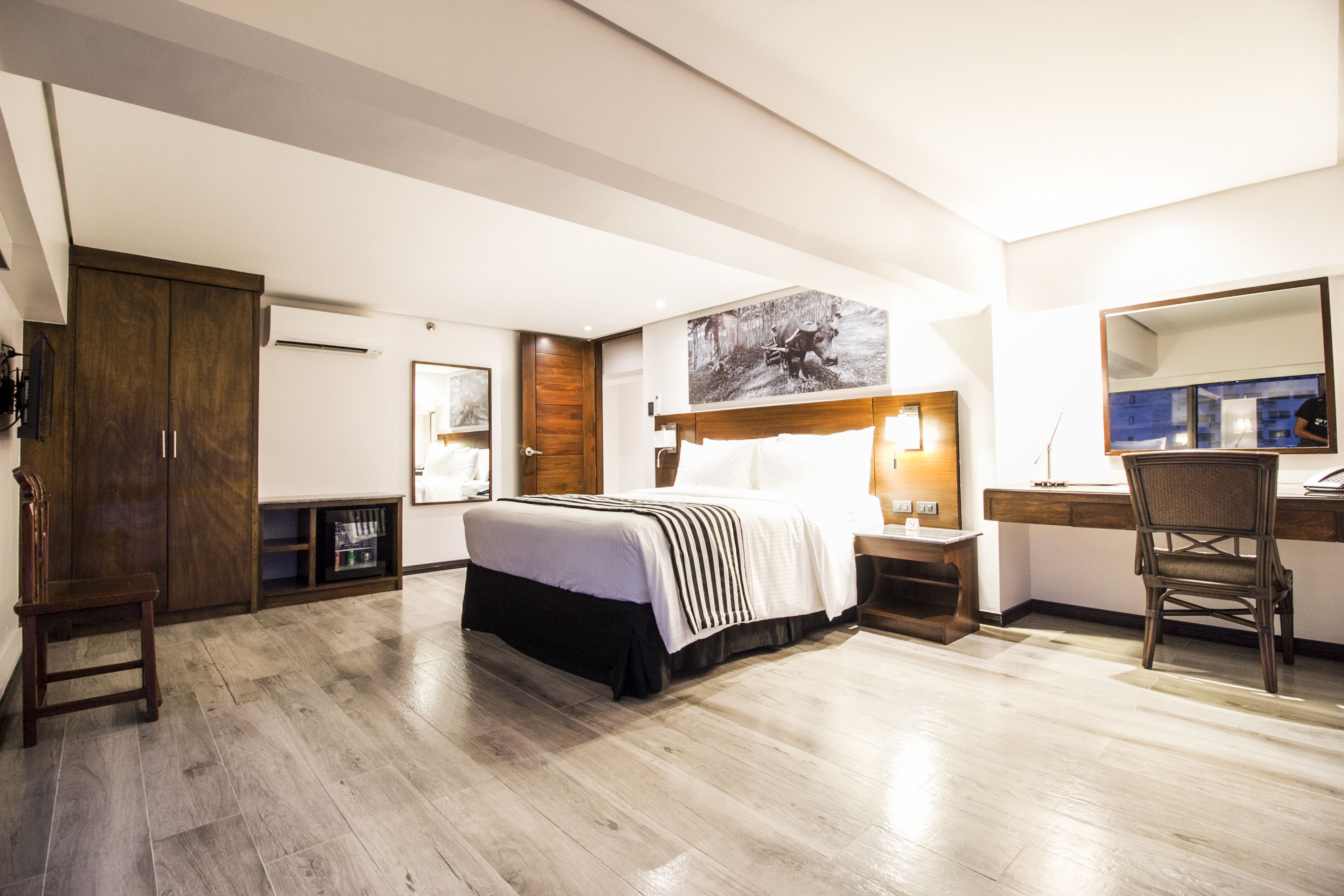 Ein Hotelzimmer mit Bett, Schreibtisch, Stuhl, Kleiderschrank und Bildern an der Wand.