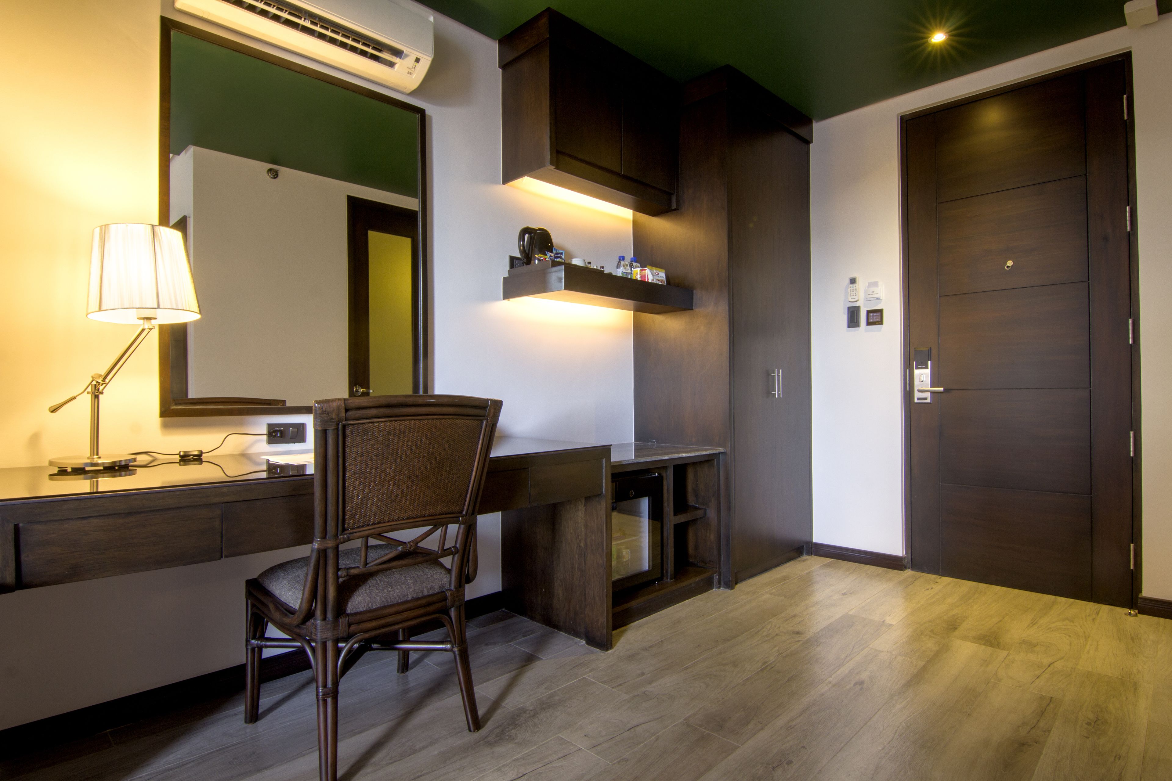 A modern hotel room with a wooden desk, a chair, a large mirror, and a wardrobe.