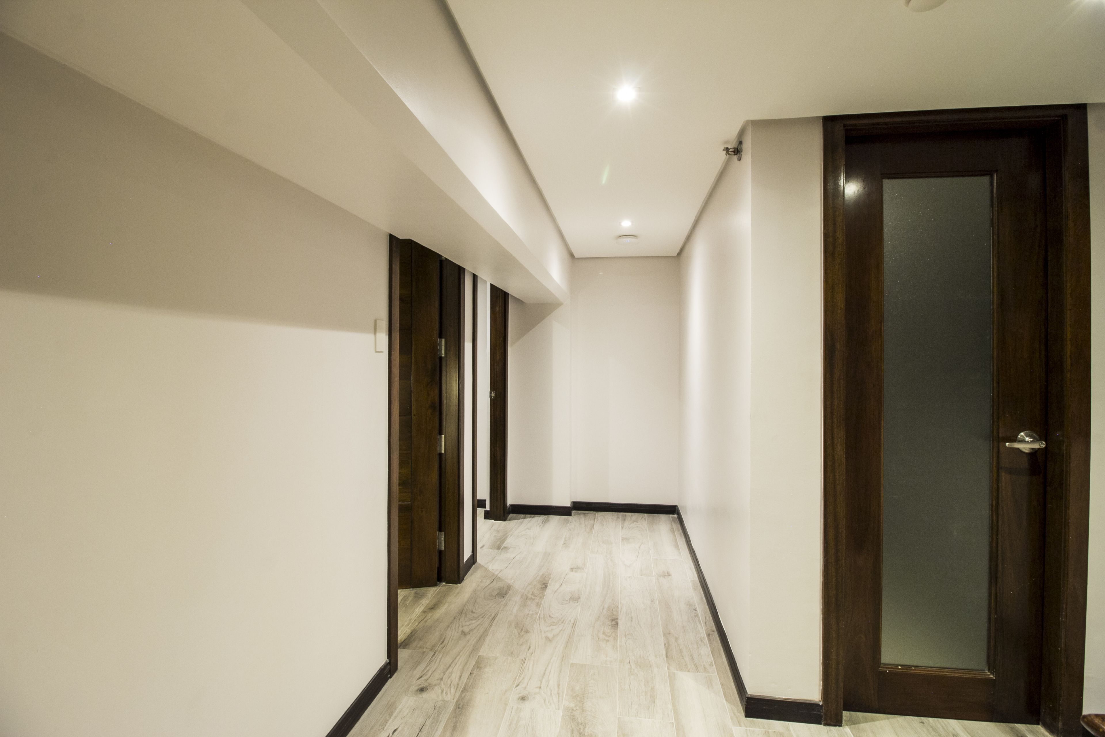 A hallway with a wooden floor, white walls, and a wooden door with a frosted glass panel.