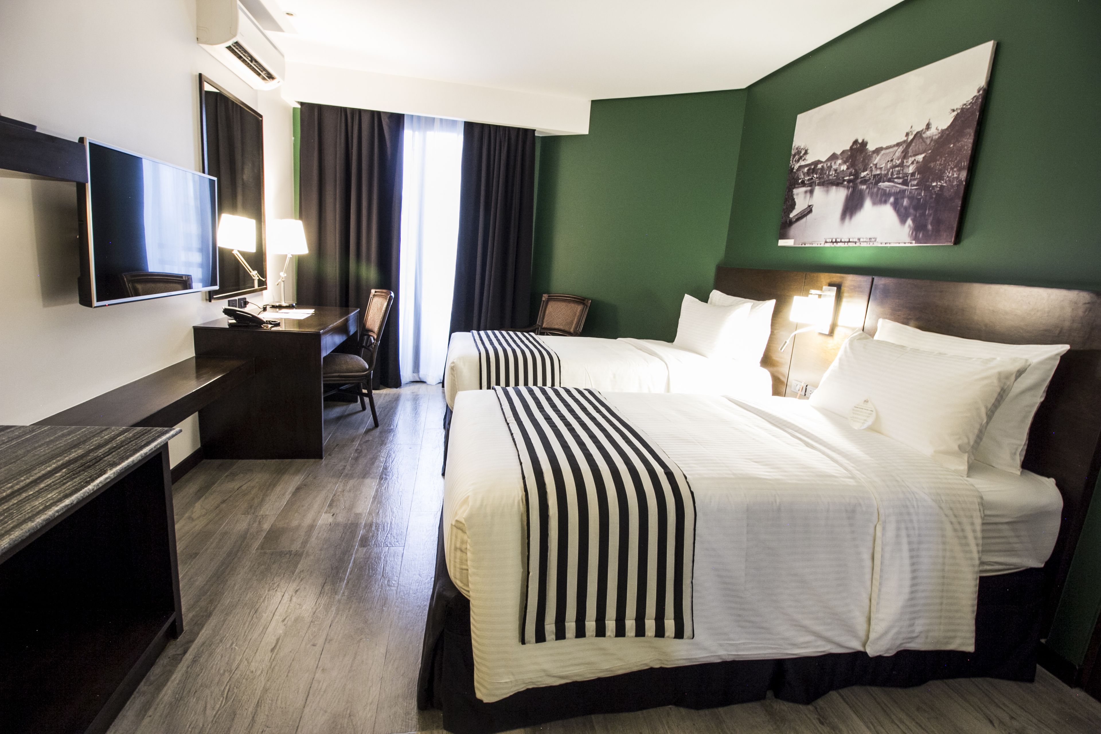 Une chambre d’hôtel avec deux lits, un bureau, une télévision et un tableau au mur.