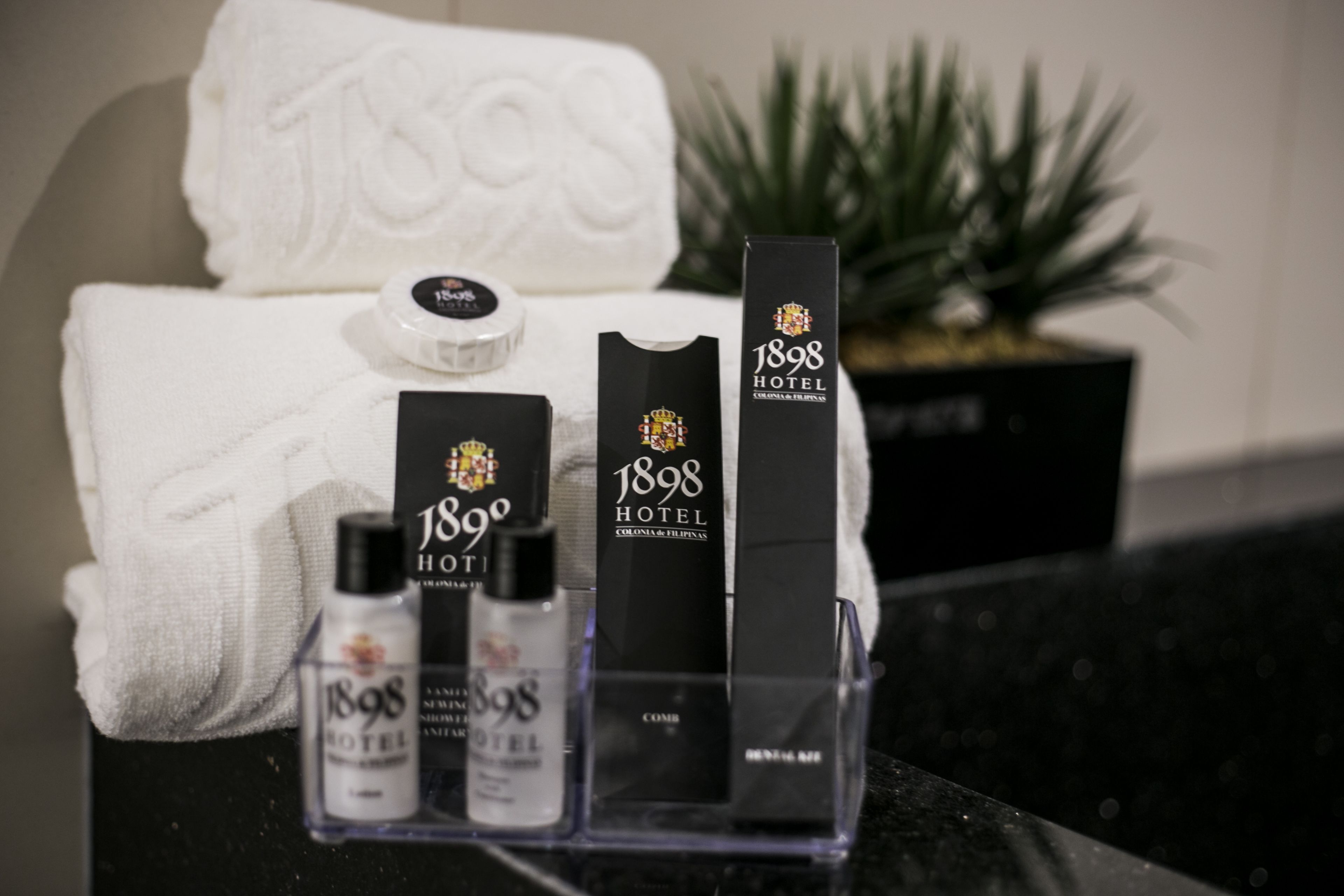 A display of 1898 Hotel branded toiletries and a towel on a counter.