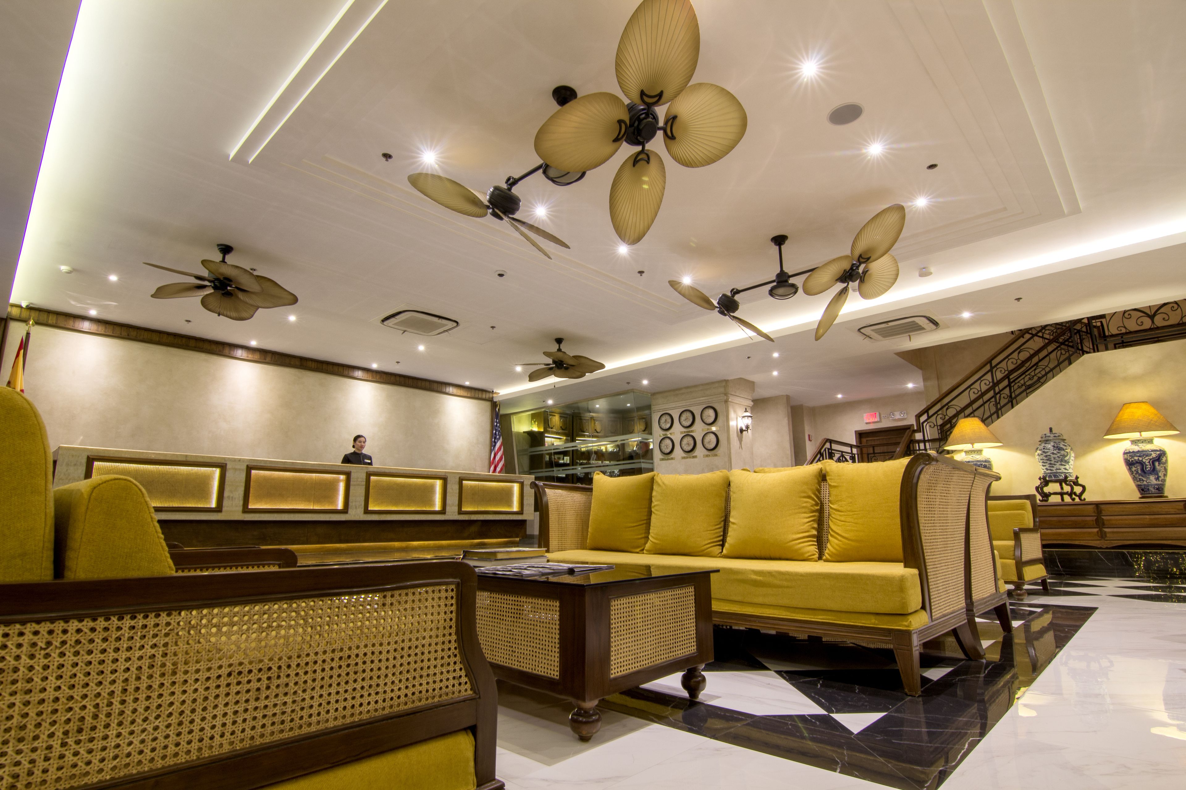A hotel lobby with multiple seating areas, ceiling fans, and a staircase.