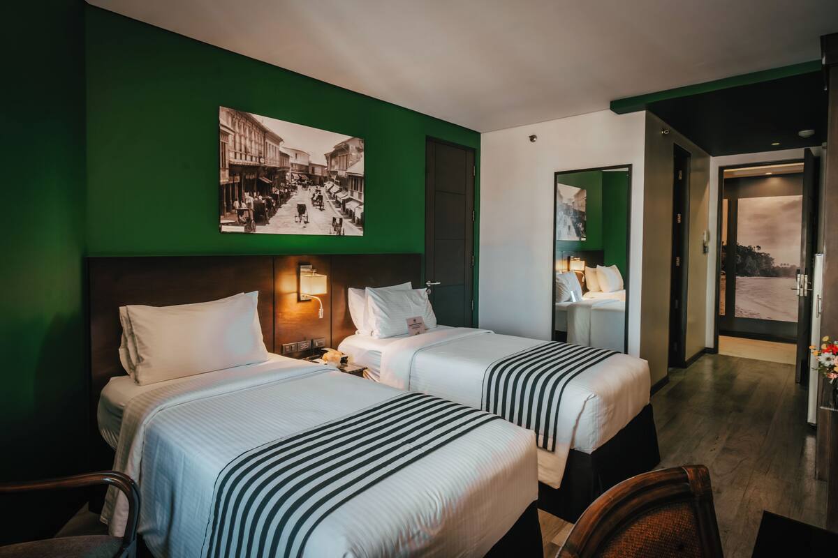 Une chambre d’hôtel avec deux lits, un mur vert et une grande fenêtre.