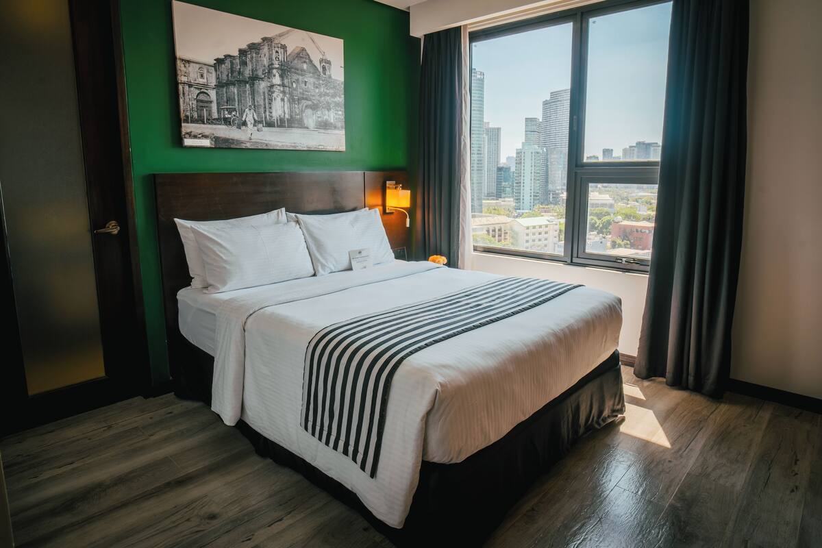 Une chambre d’hôtel avec un grand lit, une vue sur la ville, un mur végétal et un tableau encadré.