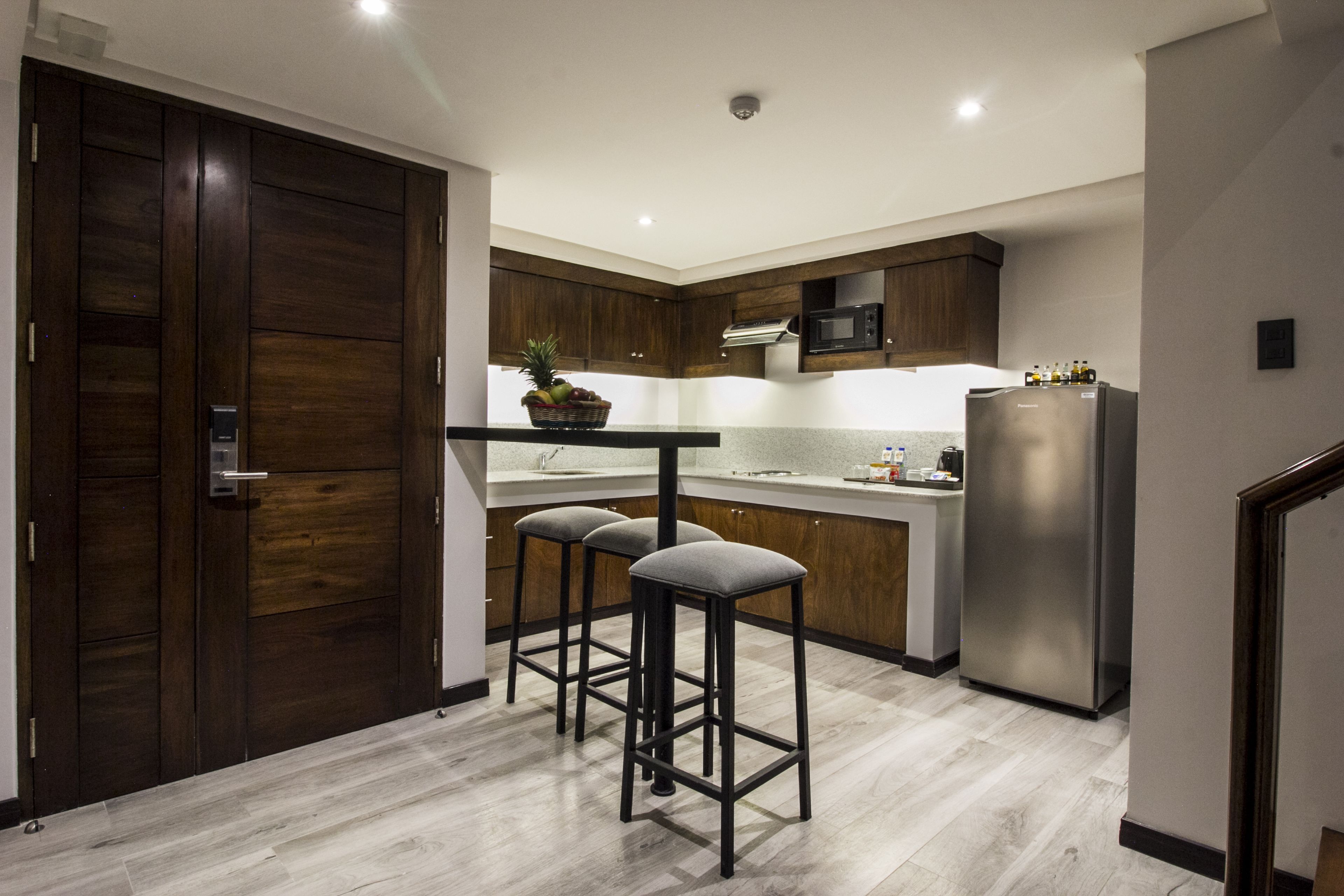 Une cuisine moderne avec des meubles de rangement en bois foncé, un réfrigérateur en acier inoxydable et un coin bar avec des tabourets.