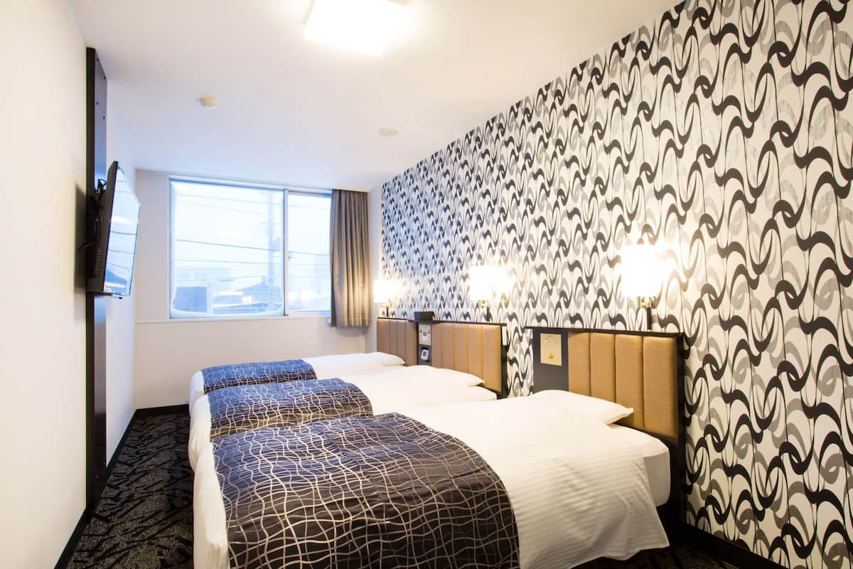 A hotel room with two beds, a TV, a window, patterned wallpaper, and wall-mounted lamps.