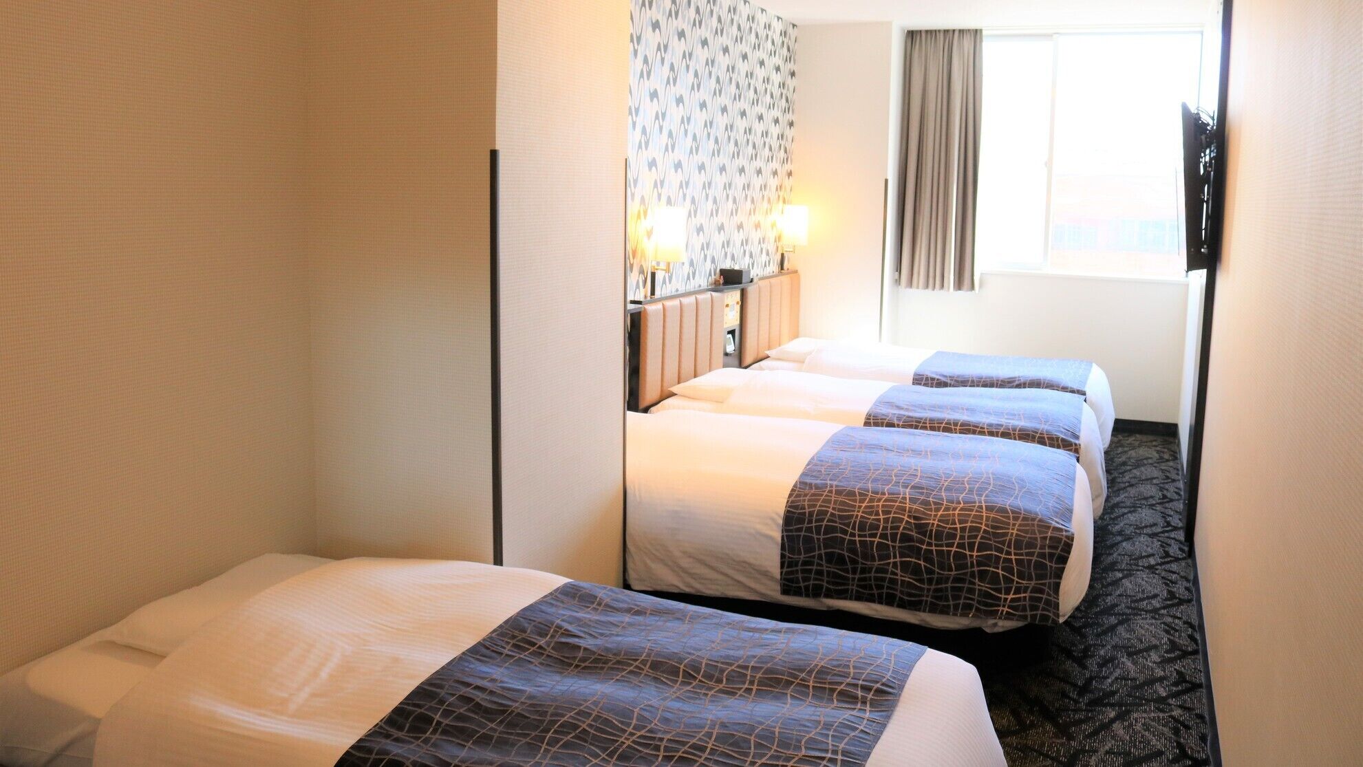 Une chambre d’hôtel avec deux lits, un mur décoré de motifs, une fenêtre avec des rideaux et un téléviseur fixé au mur.