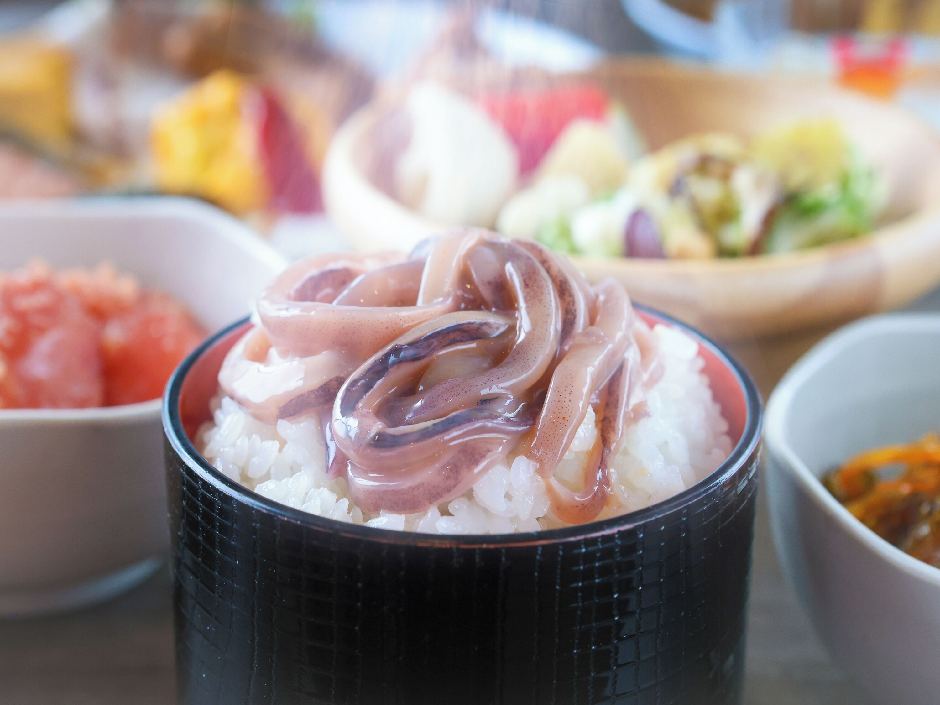 A bowl of rice topped with a pinkish translucent topping, possibly a type of seafood or vegetable.