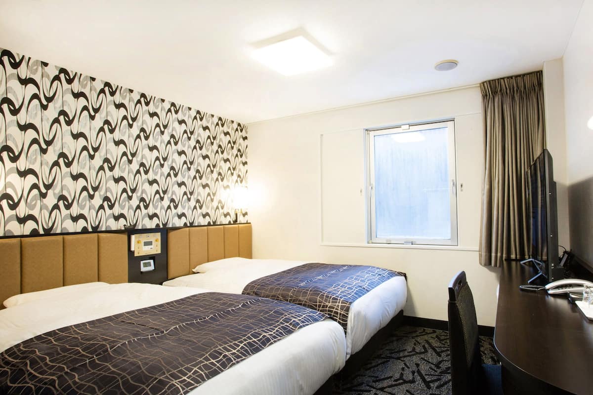 A hotel room with two beds, a desk, a chair, a TV, and a window with curtains.