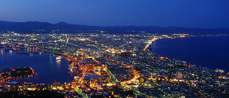 Un paisaje urbano nocturno con un muelle, edificios iluminados y un puente.