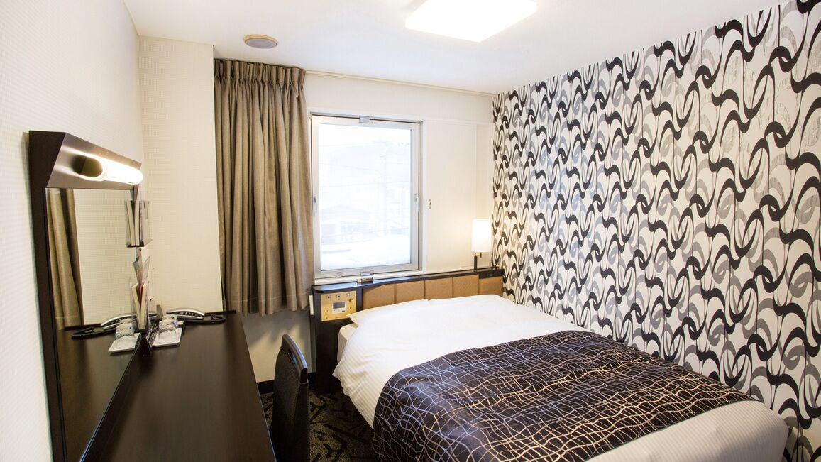 Une chambre d’hôtel avec un lit, un bureau doté d’un miroir, une fenêtre avec des rideaux et un mur orné d’un motif.