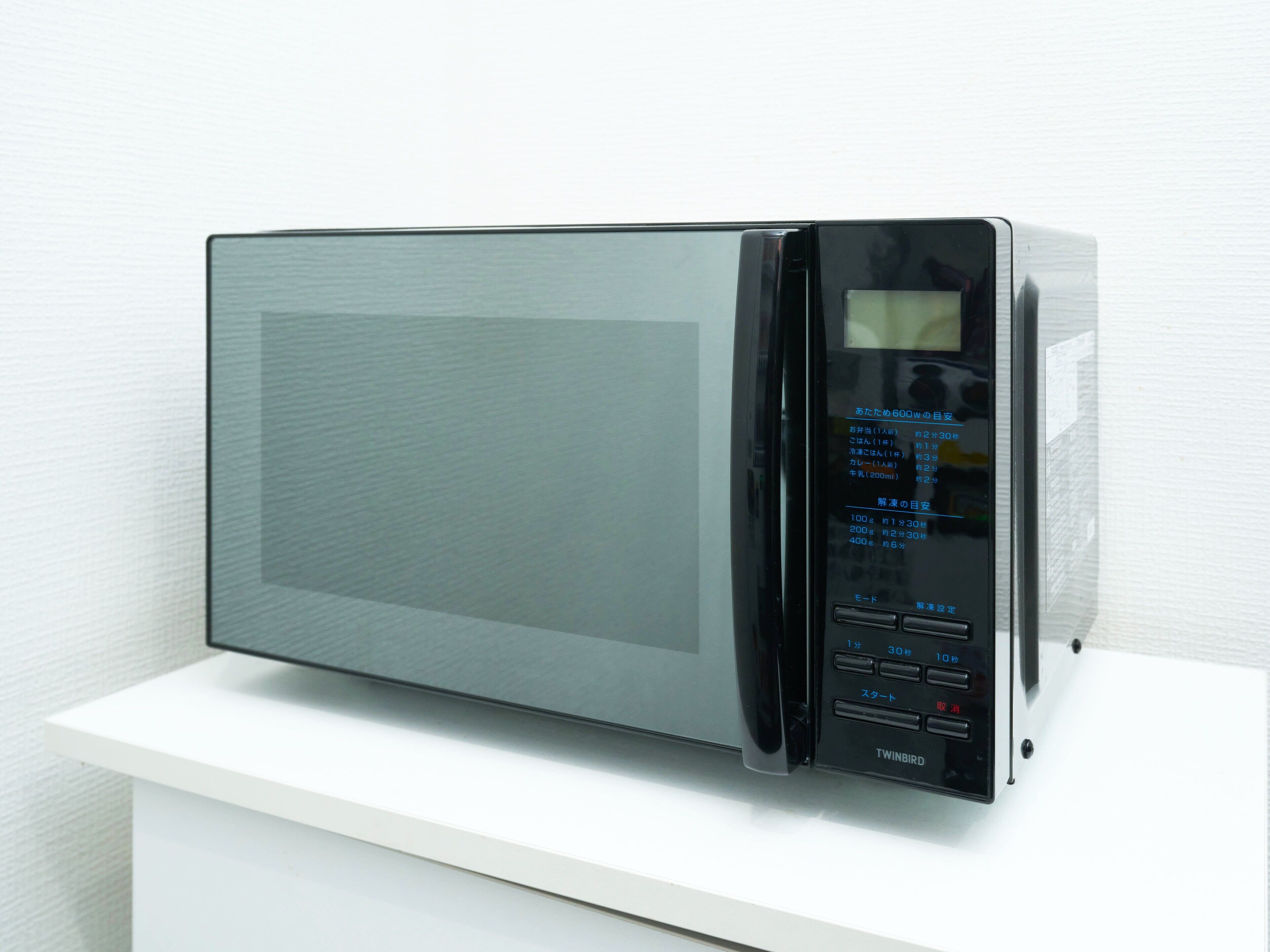A modern microwave with a digital display, placed on a white surface.