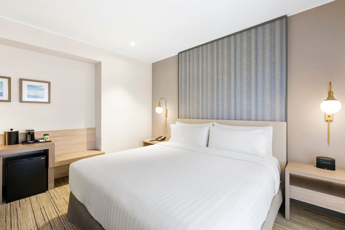 A hotel room with a large bed, a desk with a coffee machine, a phone, and a small refrigerator.