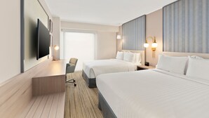 Habitación de hotel con dos camas, un escritorio, una silla, un televisor y un ventanal grande.