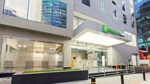 Un edificio moderno con un letrero de Holiday Inn Express, con fachada de vidrio, zona de estar al aire libre y una entrada bien iluminada.