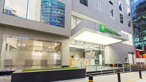 A modern building with a Holiday Inn Express sign, featuring a glass facade, outdoor seating area, and a well-lit entrance. - Holiday Inn Express Lima San Isidro by IHG (Lima)