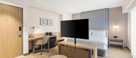 Ein Hotelzimmer mit Bett, Schreibtisch mit Flachbildfernseher, Sofa, kleinem Tisch und Nachttischlampe.