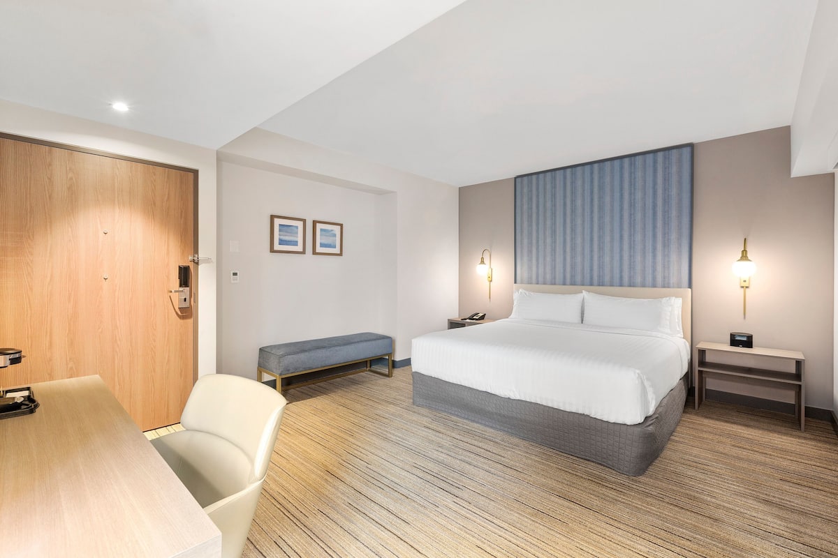 A hotel room with a bed, bedside tables, a desk, and a bench.