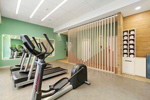 Una sala de gimnàstica amb cintes de córrer, una bicicleta estatica i una màquina d'aixetes. Hi ha una paret de fusta amb prestatges i un mirall.
