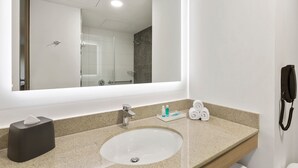 Un baño con un espejo grande, un lavabo, un perchero para toallas y un teléfono.