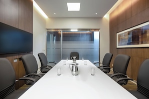 Una sala de conferències amb una taula llarga, cadires, una pantalla de projector i un separador de vidre.