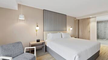 Una habitación de hotel moderna con una cama grande, una mesita de noche, una silla y un área de ducha.