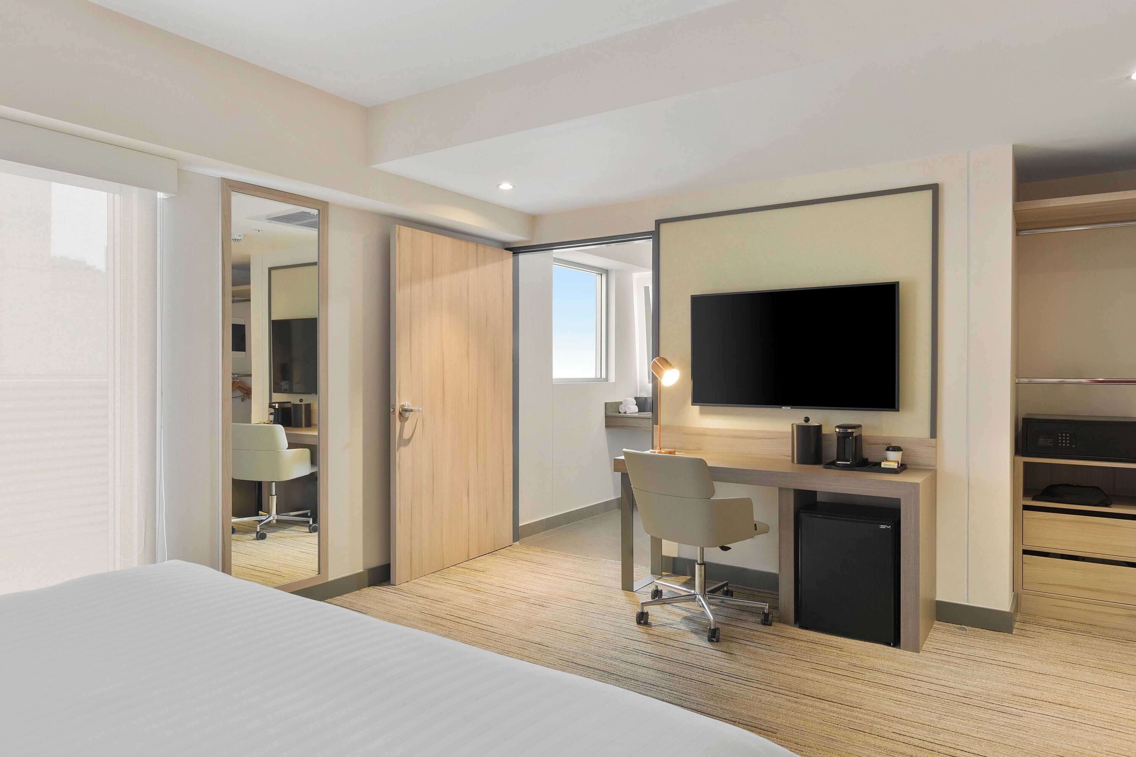 Habitación de hotel con cama, escritorio, televisor, armario y un refrigerador pequeño.