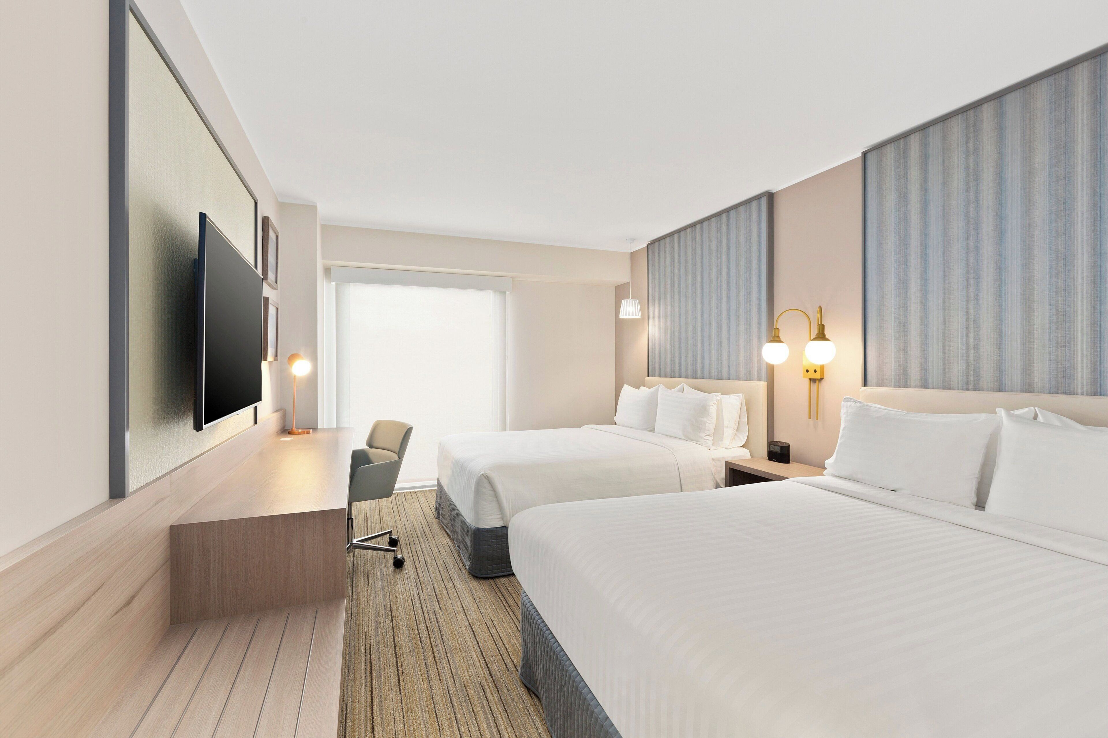 Een hotelkamer met twee bedden, een bureau, een stoel, een televisie en een groot raam.