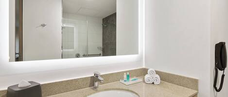 Un baño de hotel con un espejo grande, un lavamanos, un perchero para toallas y un teléfono.