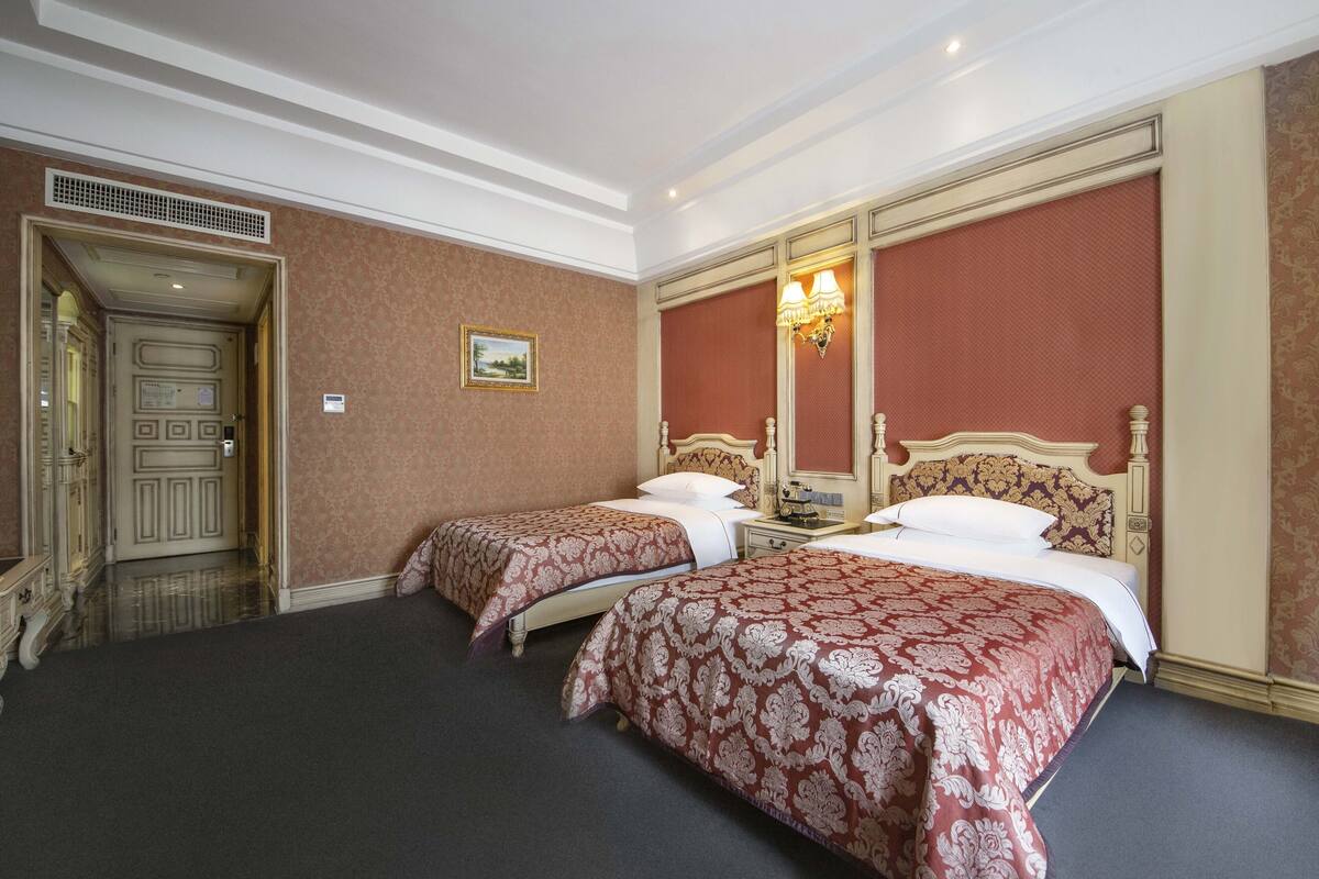 A hotel room with two beds, a large mirror, a chandelier, and a door leading to a hallway.