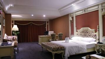 A hotel room with a large bed, a desk, a chair, a bench, and a desk lamp.