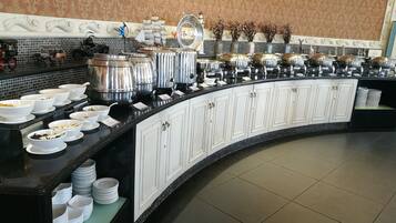 A buffet setup with multiple food stations, white cabinets, and a tiled floor.