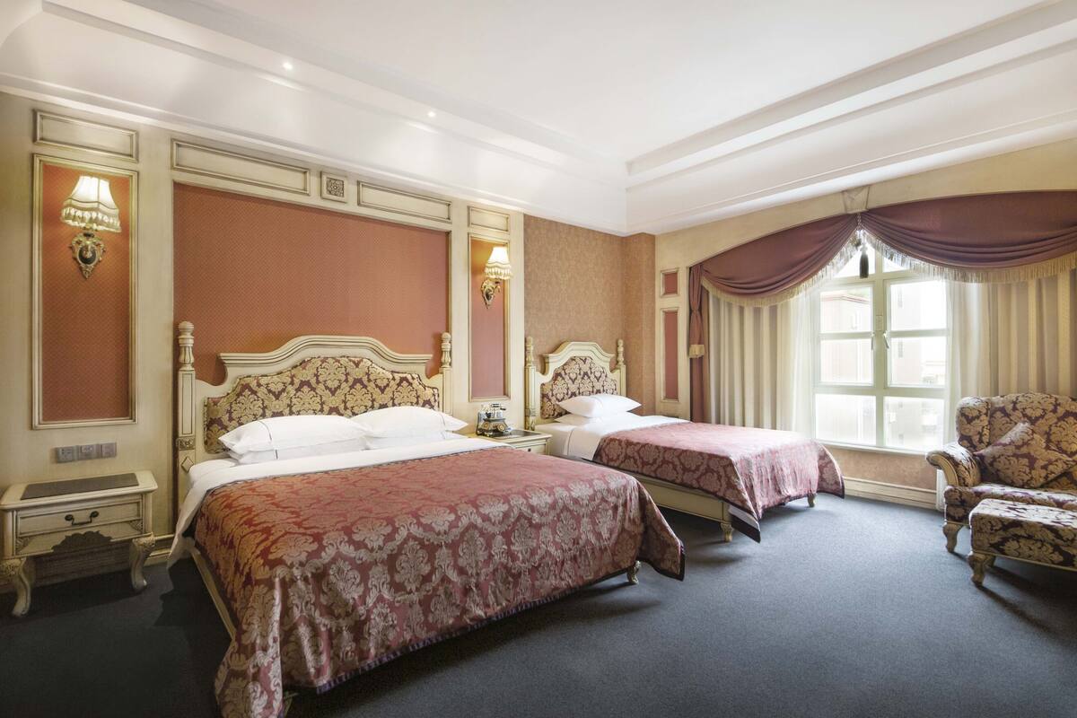 A hotel room with two beds, a chair, and a window with curtains.