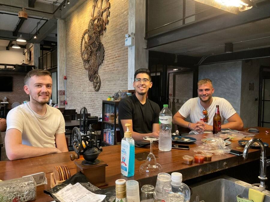 A bar area with three people seated at a counter, a large wall clock, and various bar tools and bottles.