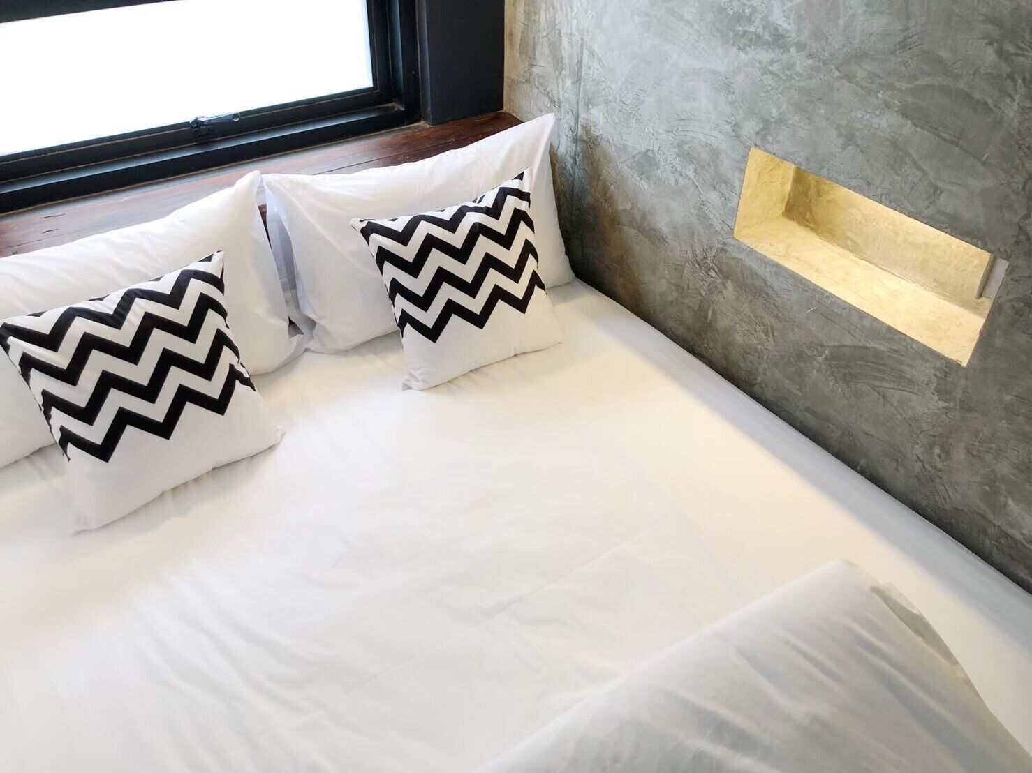 A bed with white bedding and three pillows with black zigzag patterns.